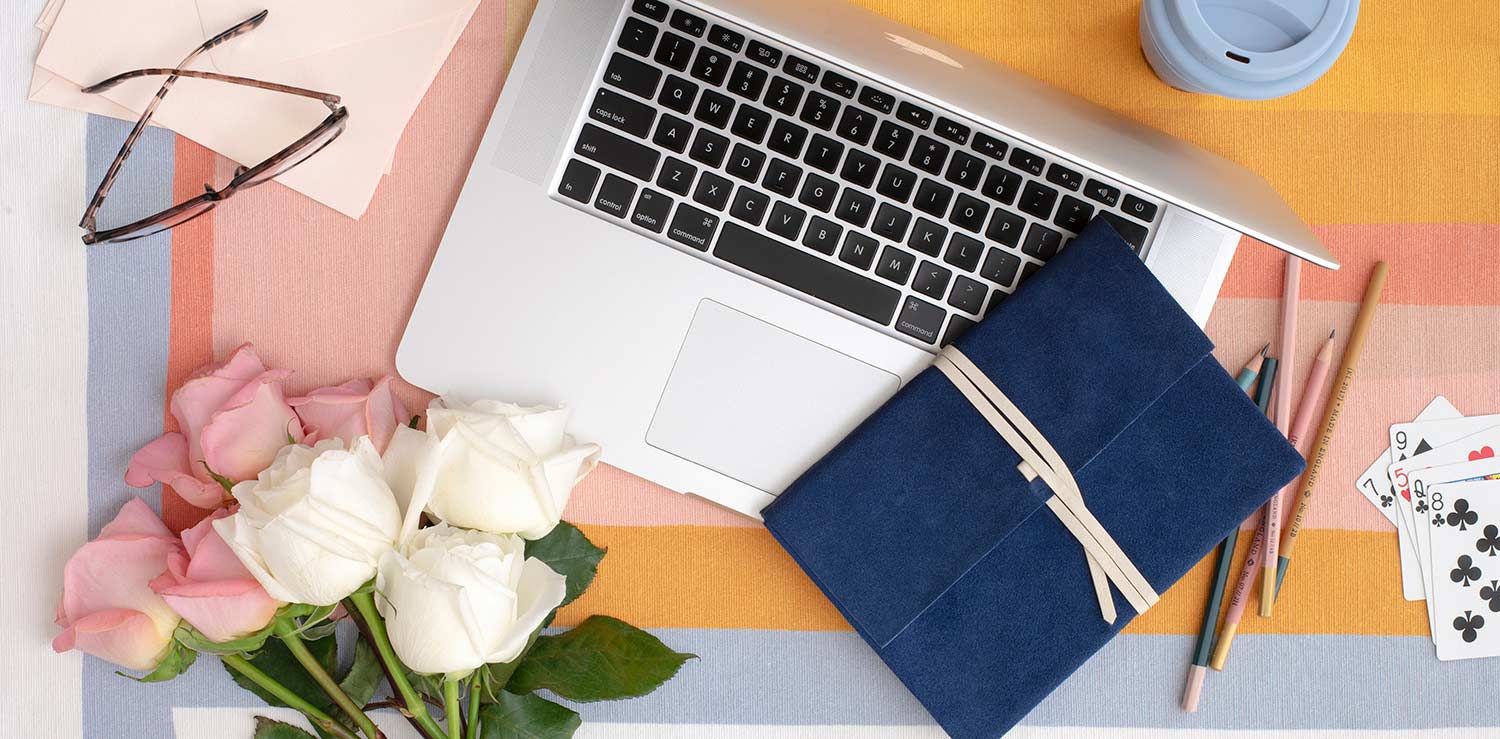 laptop and notebook on a colorful desk, with white roses