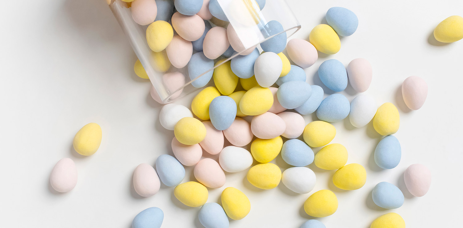 Pastel color chocolate eggs spilling out of a glass jar onto a white surface