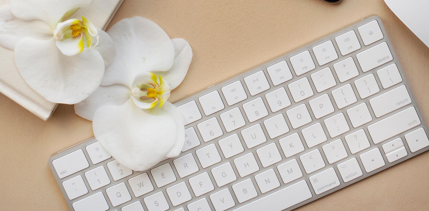 computer keyboard with white orchid flower on beige background