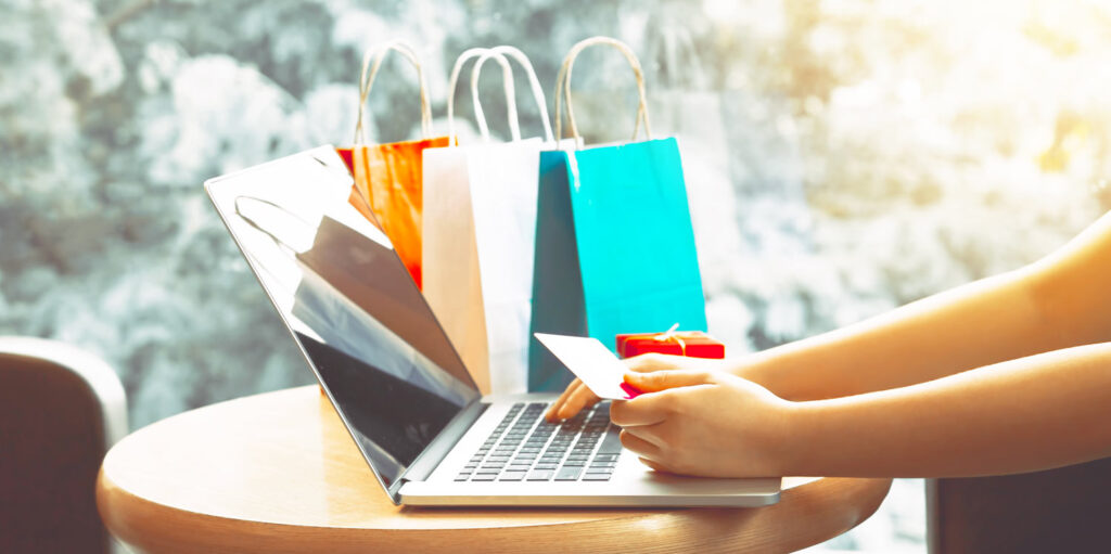 Woman at laptop with credit card and shopping bags.